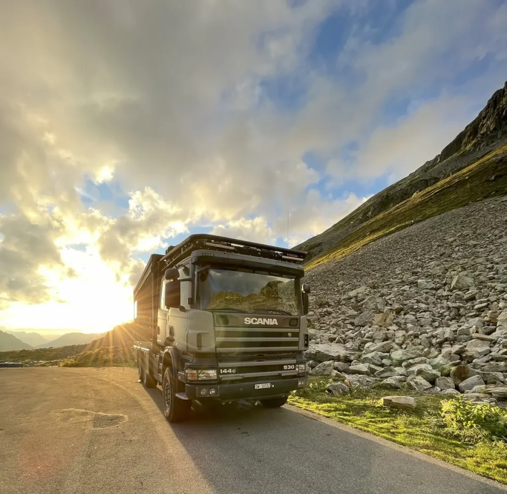 Ein modifiziertes Scania Expeditionsmobil parkt auf einer Bergstraße im Sonnenuntergang.