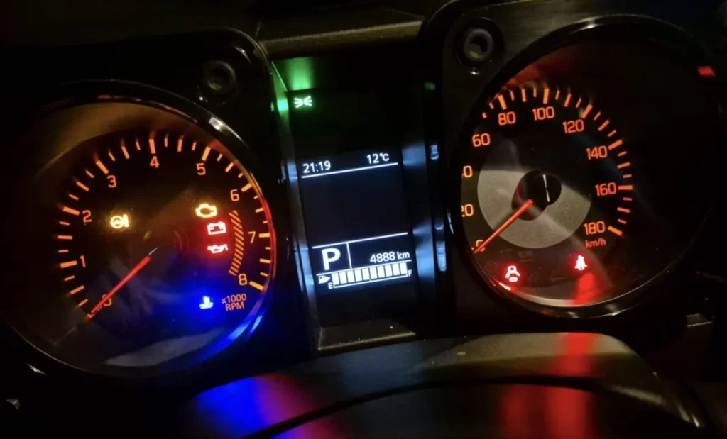 Ein beleuchtetes Auto-Armaturenbrett bei Nacht mit Tachometer, Kilometerstand und Warnleuchten.