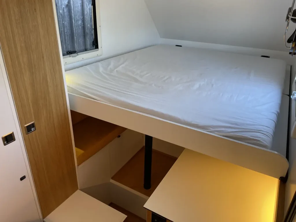 Heller Campervan-Innenraum mit Hochbett, integrierter Holztreppe und cleverem Stauraum.