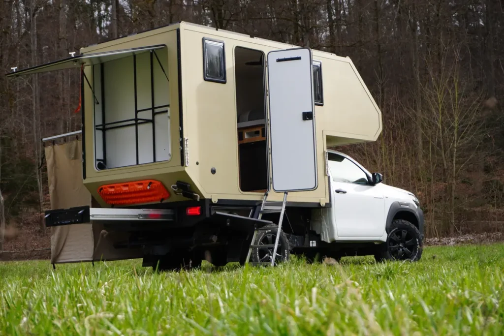 Offroad-Pick-up mit beiger Wohnkabine, geöffneter Heckklappe, Einstiegsleiter und ausgefahrenem Heckauszug.