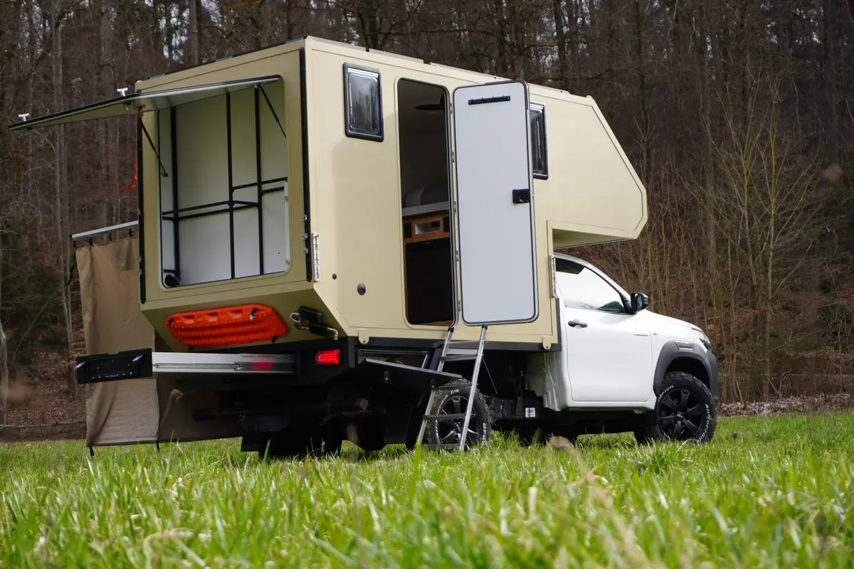 Offroad-Pick-up mit beiger Wohnkabine, geöffneter Heckklappe, Einstiegsleiter und ausgefahrenem Heckauszug.