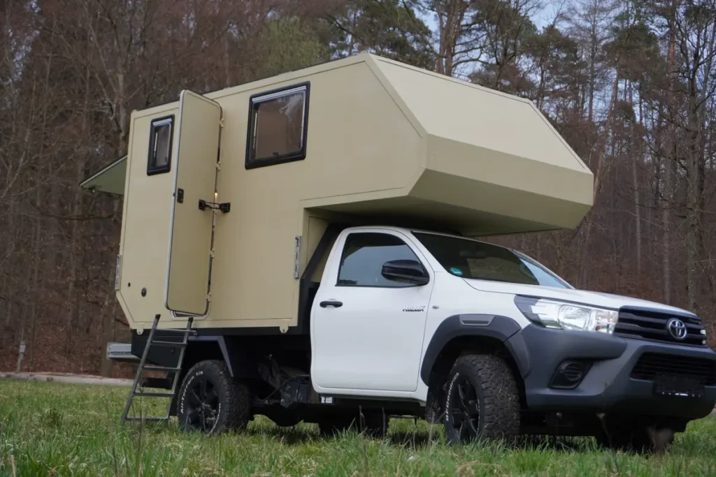 Robustes Expeditionsmobil mit beiger Wohnkabine auf einem weißen Toyota Hilux Pick-up.
