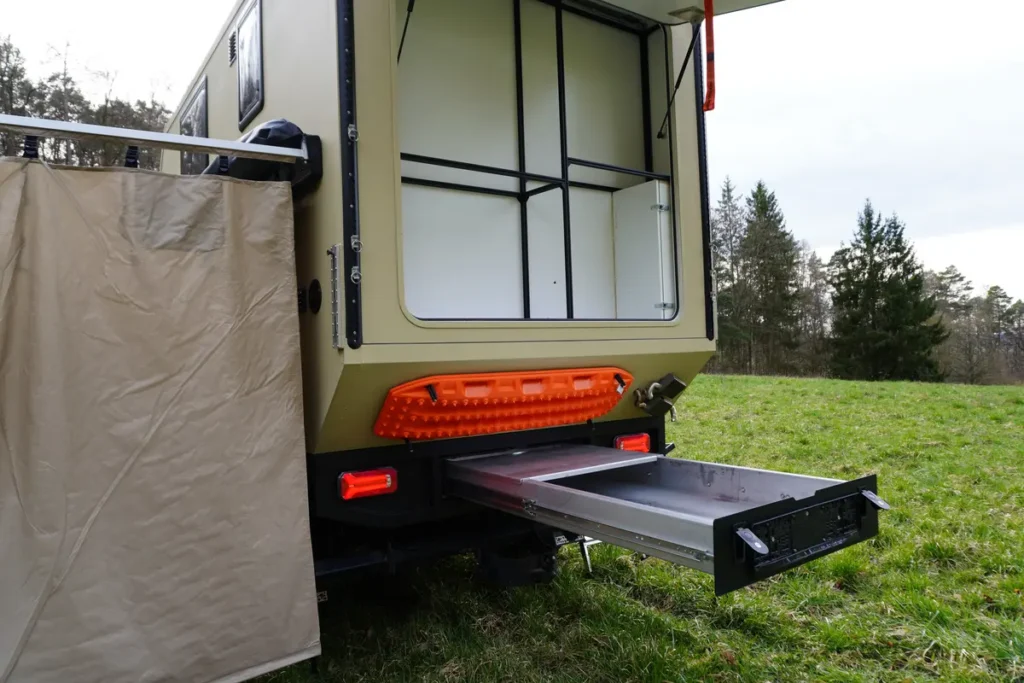 Rückansicht eines Expeditionsmobils mit geöffnetem Stauraum, Heckauszug, Sandblech und Duschzelt.