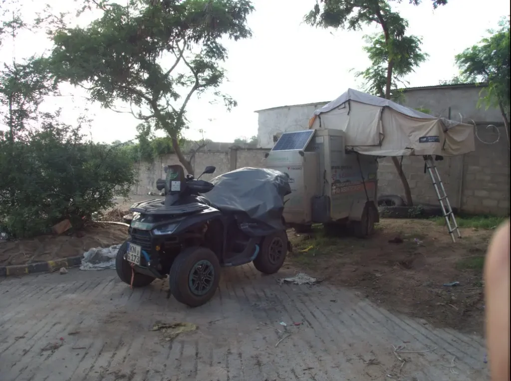 Ein geparktes ATV steht vor einem Campinganhänger mit aufgebautem Dachzelt und Solarmodul.
