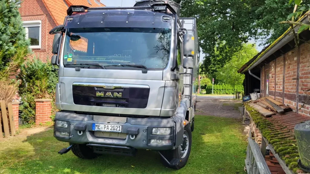 Silberner MAN Allrad-LKW als Expeditionsmobil auf einer grünen Wiese geparkt.