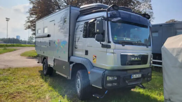 Silbernes MAN Allrad-Expeditionsmobil mit Wohnkabine auf einer grünen Wiese.