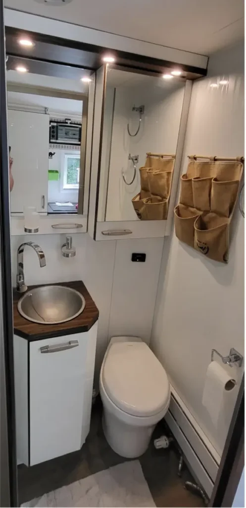 Kompakte Nasszelle im Campervan mit Waschbecken, Toilette und Spiegelschrank.