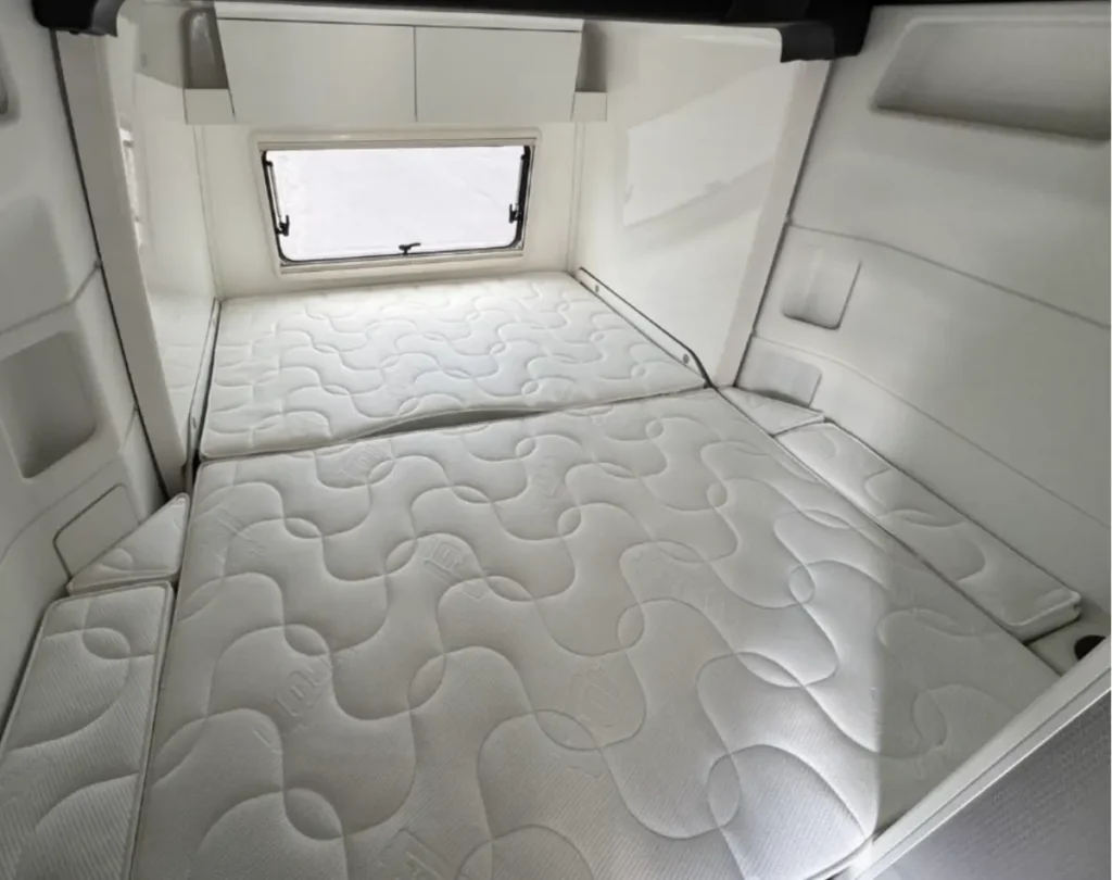 Großes Bett mit mehreren Matratzenelementen und Fenster im Wohnmobil.