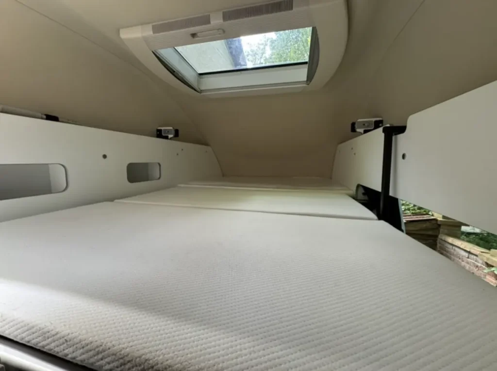 Schlafbereich in einem Campervan mit zwei Betten, Seitenwänden und Dachfenster.