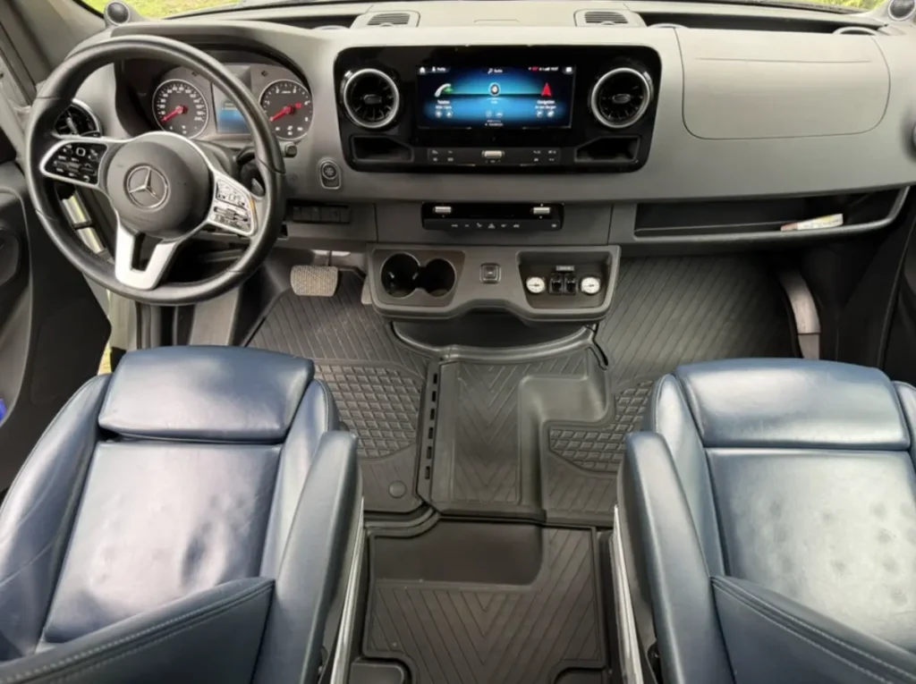 Innenansicht eines Mercedes Sprinter Campervans mit Armaturenbrett und blauen Ledersitzen.
