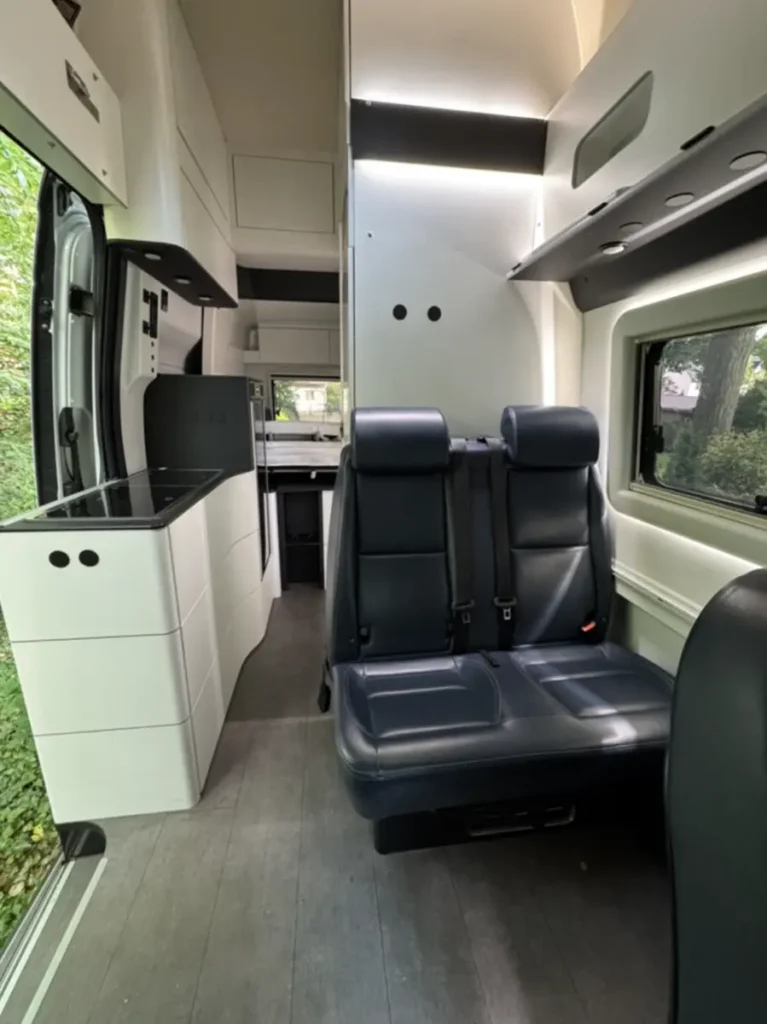 Heller Innenraum eines modernen Campervans mit integrierter Küche und dunklen Rücksitzen.