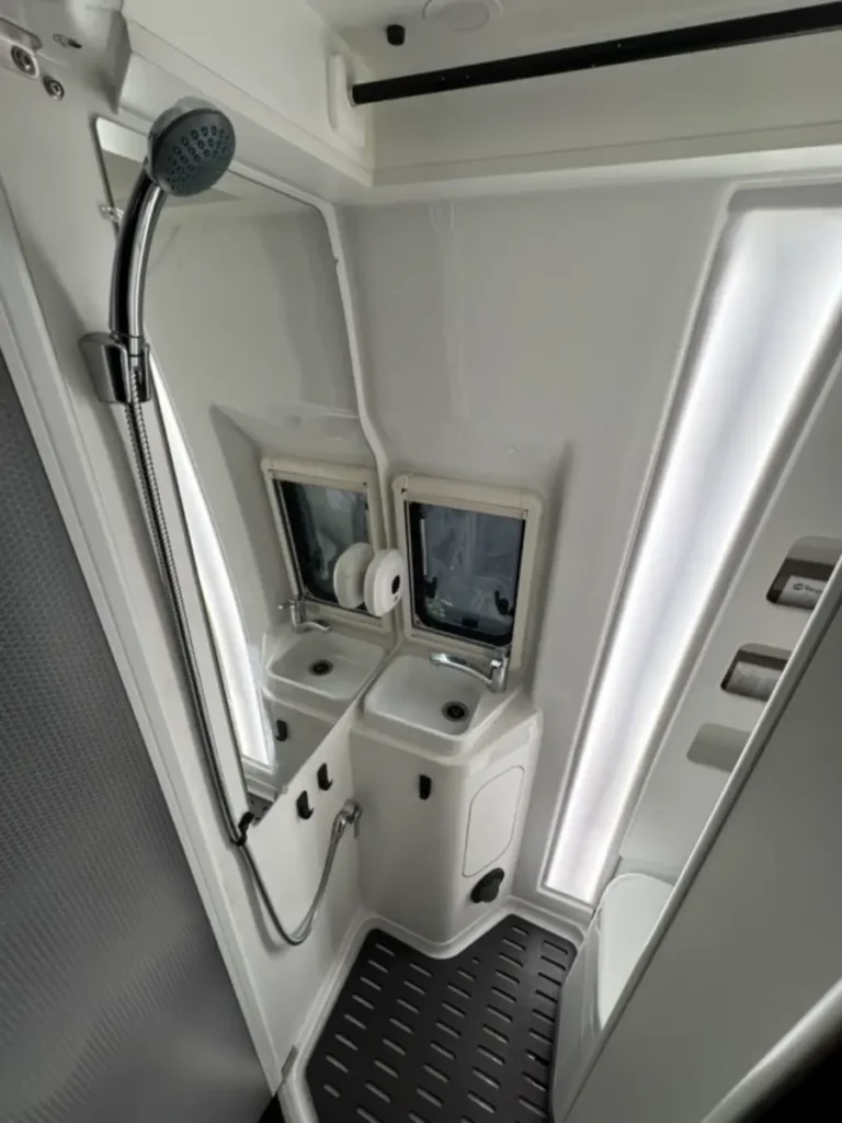 Modernes, kompaktes Campervan-Bad mit Dusche, Waschbecken, Toilette und Spiegelfläche.