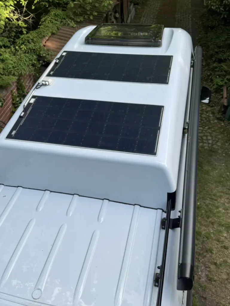 Das Dach eines weißen Selbstausbau-Campervans mit zwei flexiblen Solarmodulen und Dachluke.