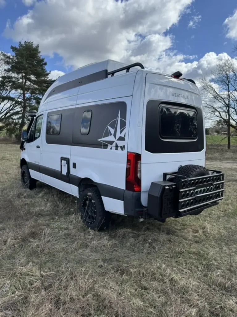 Weißer Offroad-Campervan mit Kompass-Seitenaufkleber, Dachgepäckträger und Heckträger im Gelände.