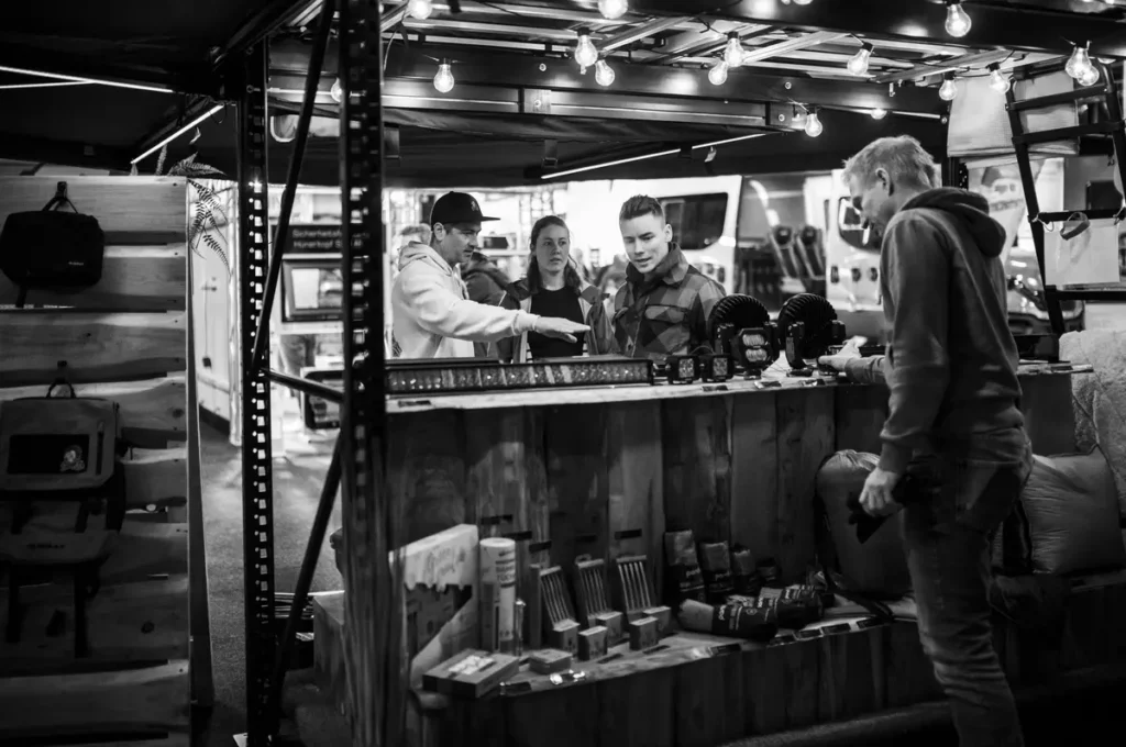 Kunden informieren sich über LED-Zusatzbeleuchtung und Offroad-Zubehör an einem Holzstand.