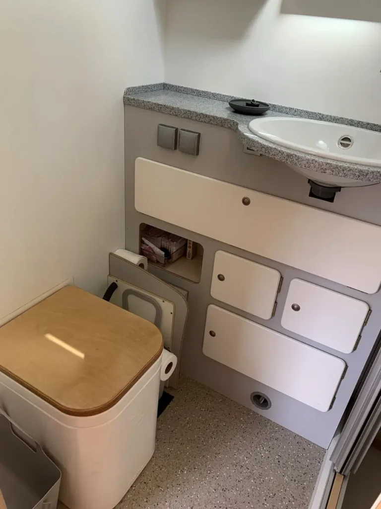 Ein modernes Campervan-Bad mit Trockentoilette, integriertem Waschbecken und cleverem Stauraum.