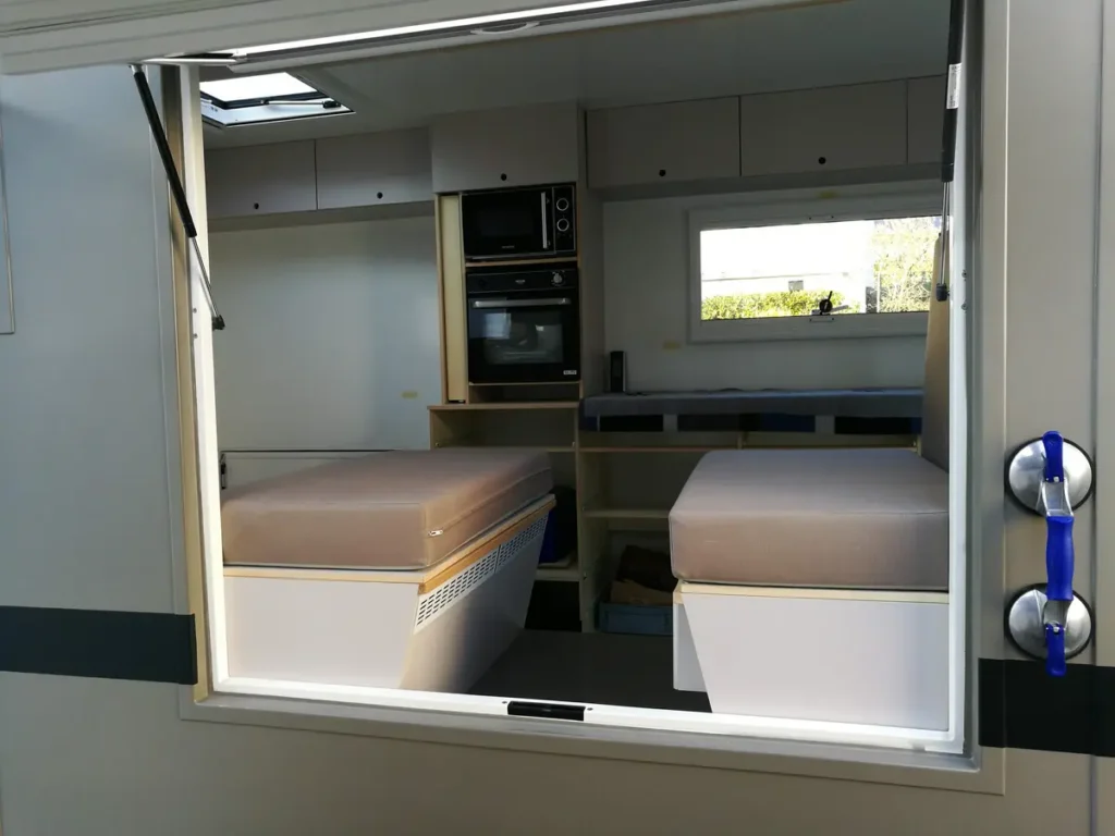 Moderner Innenausbau eines Campervans mit Küche, Betten und Dachluke, gesehen durch eine geöffnete Hecktür.
