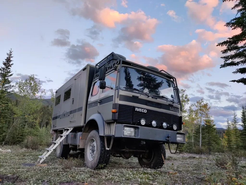 Iveco Allrad Expeditionsmobil mit individuellem Aufbau und Leiter im Abendlicht am Waldrand.