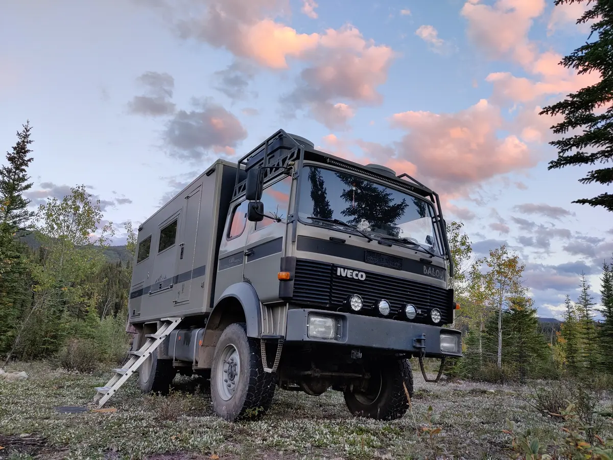 Iveco Allrad Expeditionsmobil mit individuellem Aufbau und Leiter im Abendlicht am Waldrand.