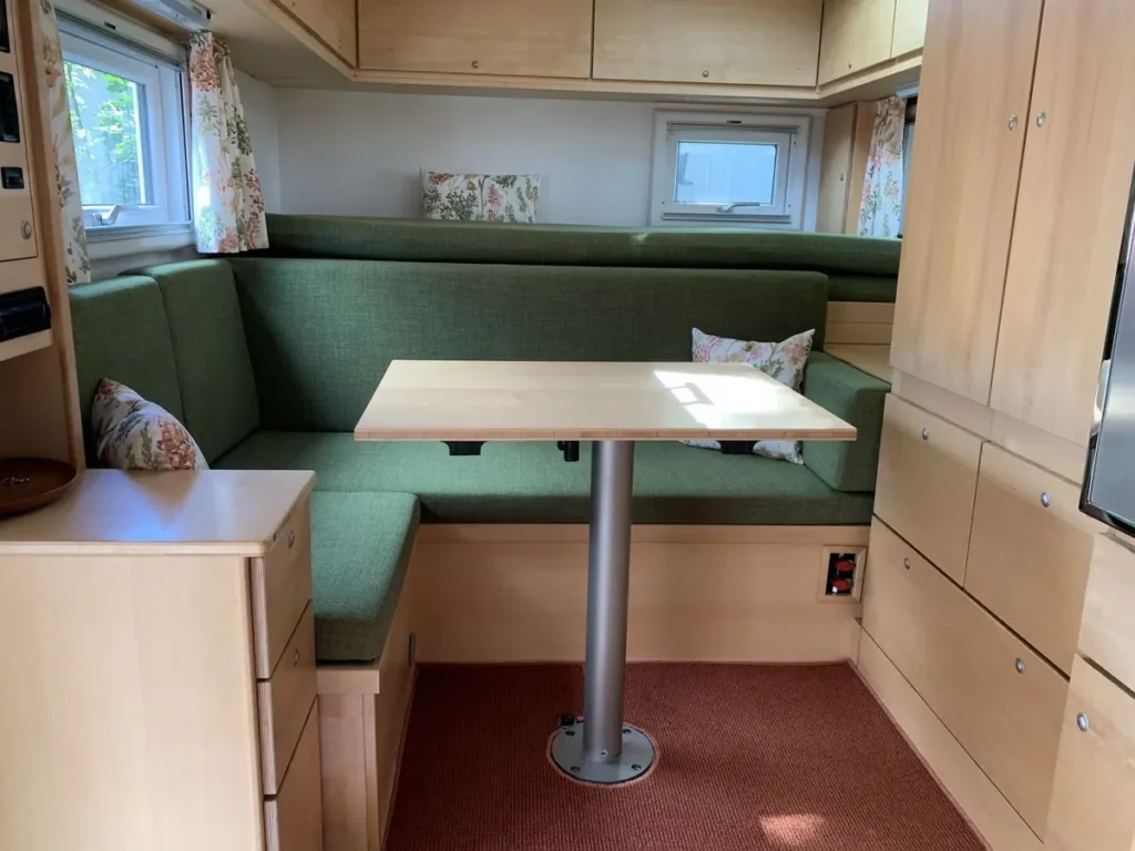 Gemütlicher Campervan-Innenausbau mit grüner Dinette und hellen Holzmöbeln.
