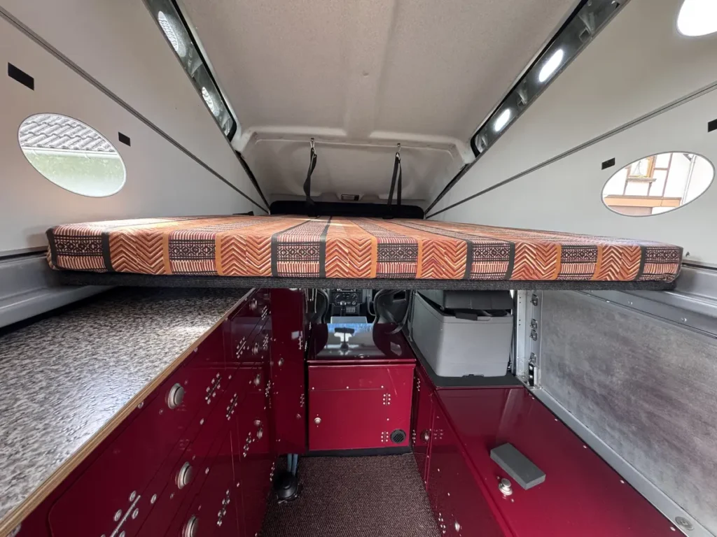 Innenansicht eines Offroad-Expeditionsmobils mit Hochbett, roten Modulen und praktischem Stauraum.