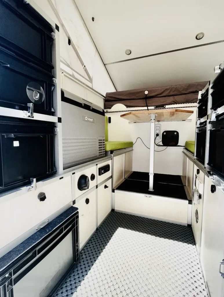 Innenansicht eines selbst ausgebauten Overlanding-Fahrzeugs mit klappbarem Tisch und modularer Einrichtung.