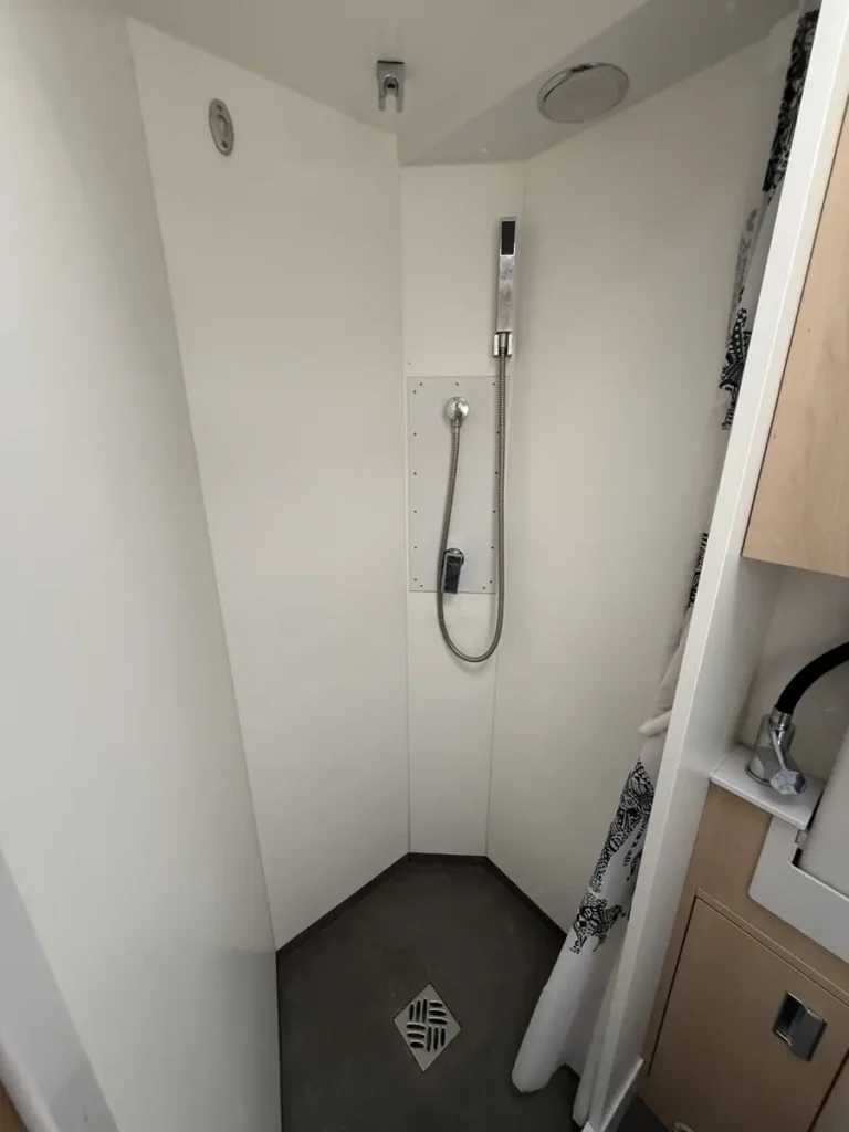 Eine kompakte Duschkabine mit Handbrause und Bodenablauf in einem Campervan.