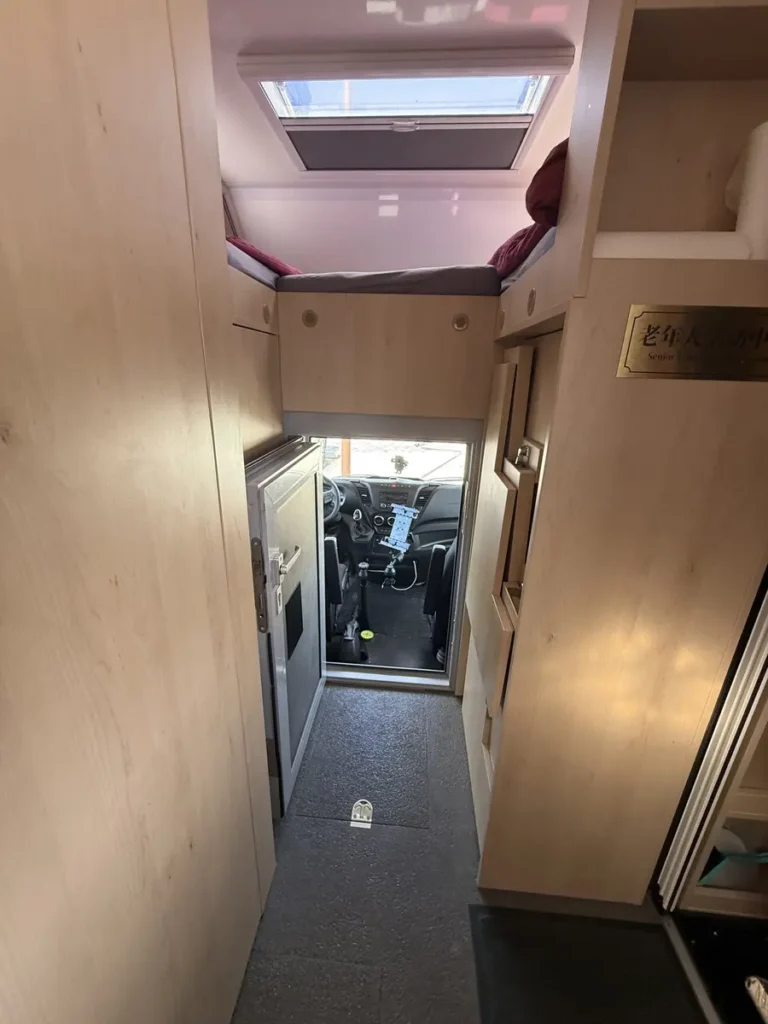Moderner Campervan-Innenausbau mit gemütlichem Alkovenbett, Dachluke und Blick ins Cockpit.