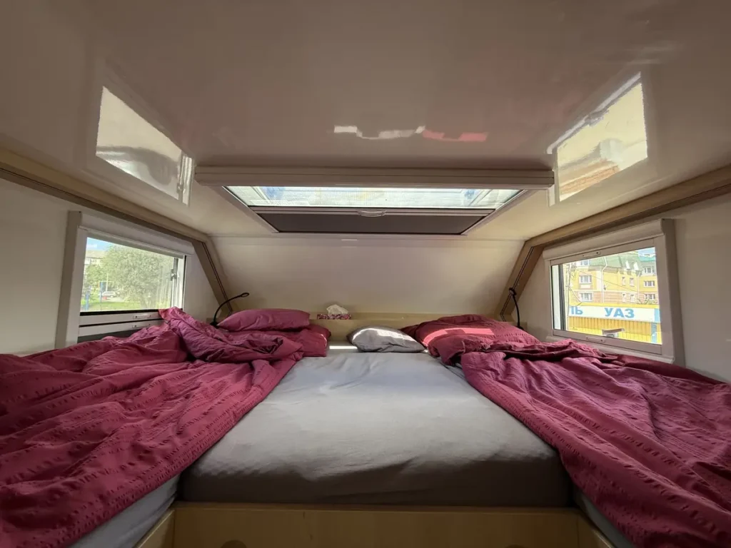 Gemütlicher Schlafbereich in einem Campervan mit zwei Betten, Dachluke und Fenstern zur Aussicht.