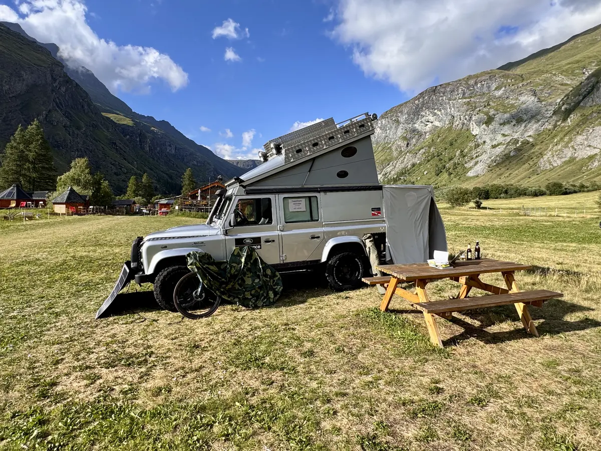 Silbernes Land Rover Expeditionsmobil mit Hubdachzelt und Solarmodulen in alpiner Berglandschaft.
