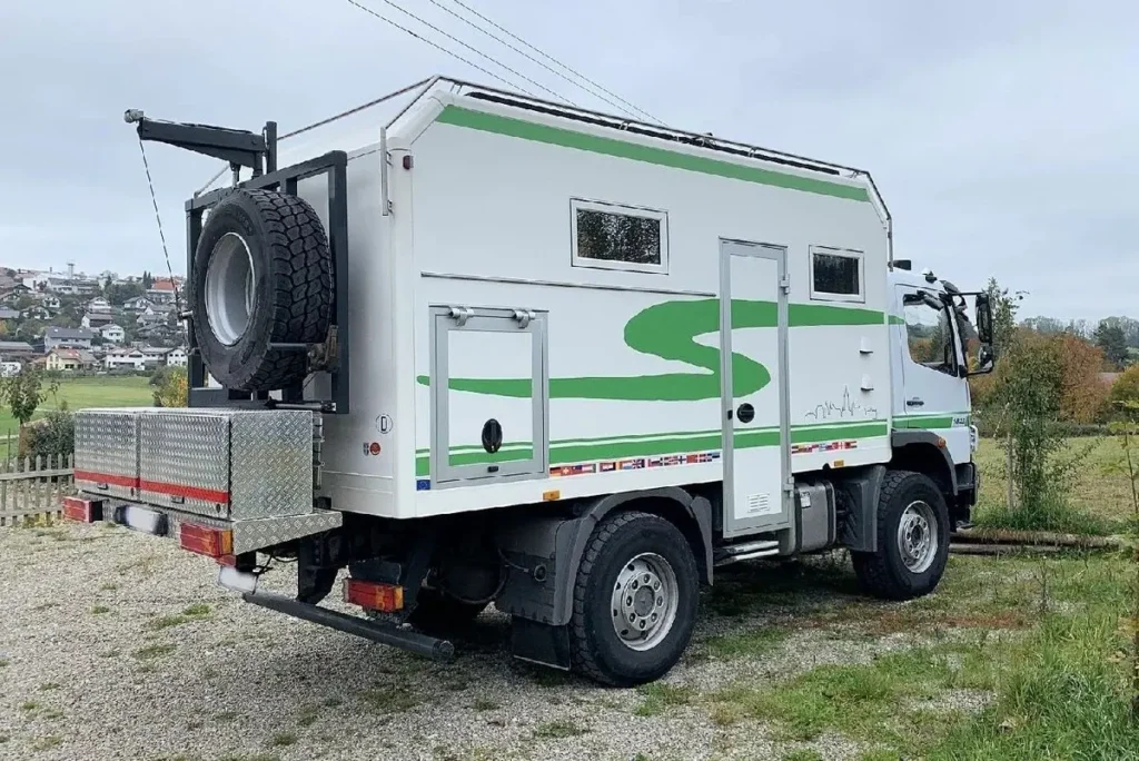 Weißes Allrad-Expeditionsmobil auf LKW-Basis mit grünen Streifen und Reserverad am Heck.