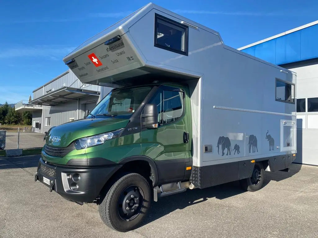 Grüner Iveco Daily 4x4 Offroad-Camper mit silbernem Expeditionsmobil-Aufbau und Schweizer Flagge.