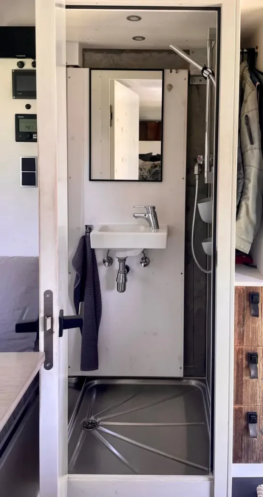 Innenansicht eines modernen Campervan-Badezimmers mit Dusche, Waschbecken und Spiegel.