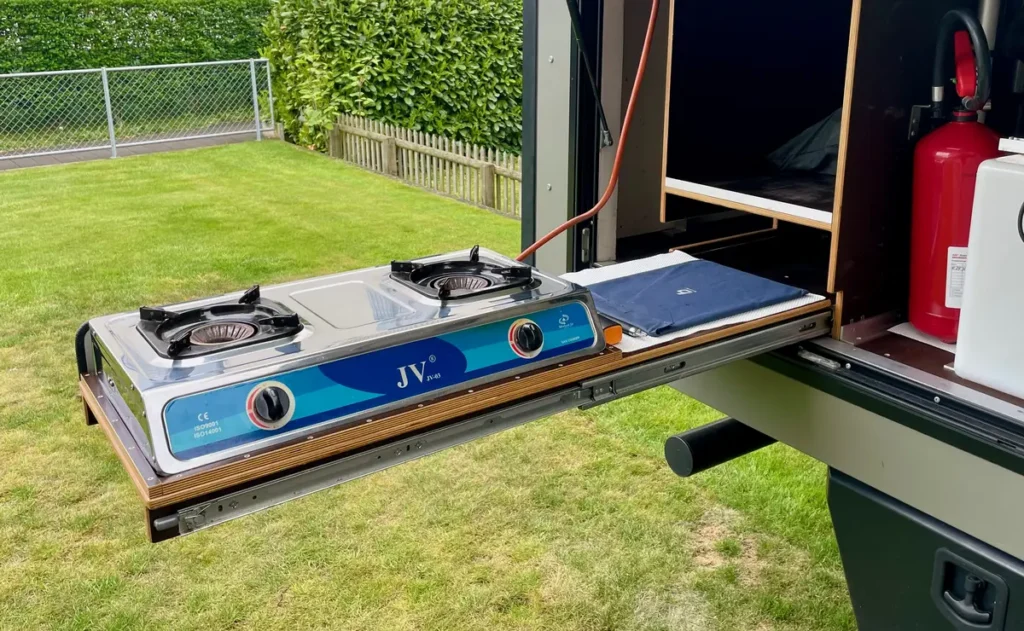Eine ausziehbare Campingküche mit Gaskocher am Campervan im Garten.