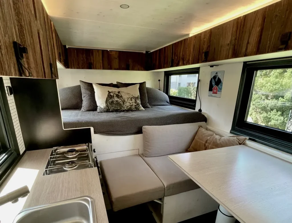 Ein heller Campervan-Innenraum mit Bett, integrierter Küche und gemütlicher Sitzgruppe.