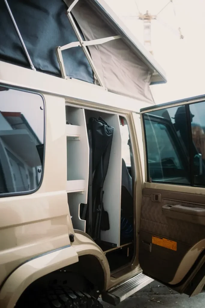 Beiges Overlander-Fahrzeug mit geöffnetem Aufstelldach und maßgeschneidertem Innenumbau zur Campernutzung.