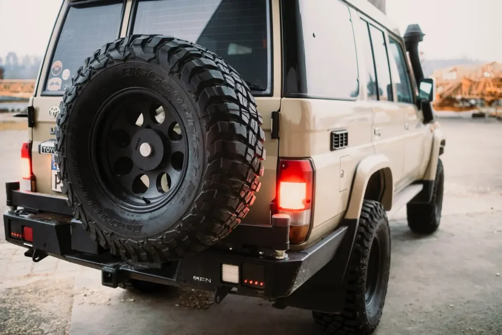 Sandfarbener Toyota Land Cruiser 4x4 mit BFGoodrich Offroad-Ersatzrad und AFN-Heckstoßstange.