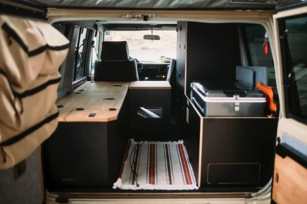 Modularer Selbstausbau in einem Overlanding-Fahrzeug mit maßgefertigten Holzmöbeln und Kühlbox.