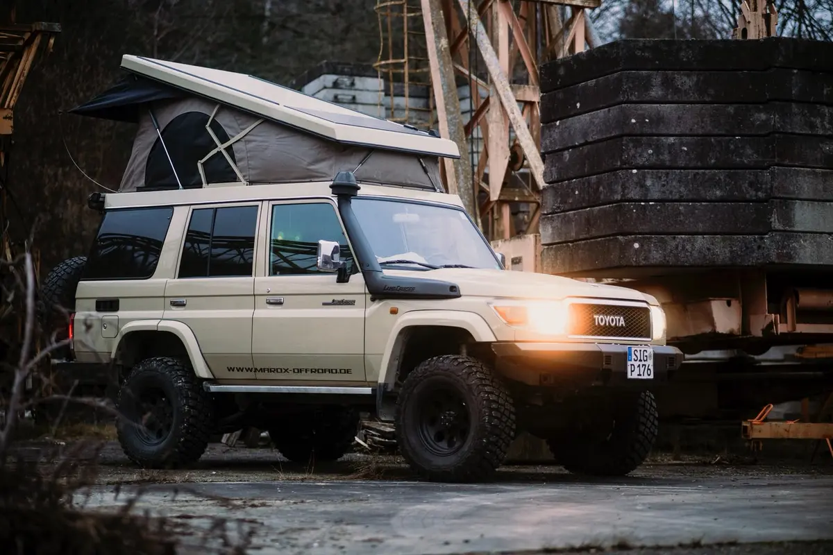 Ein helles Expeditionsmobil mit Pop-Up-Dachzelt und Schnorchel steht in einer industriellen Offroad-Umgebung.