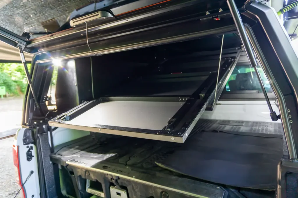 Pick-up Ladeflächenausbau mit beleuchtetem Klapptisch und geöffneter Heckklappe.
