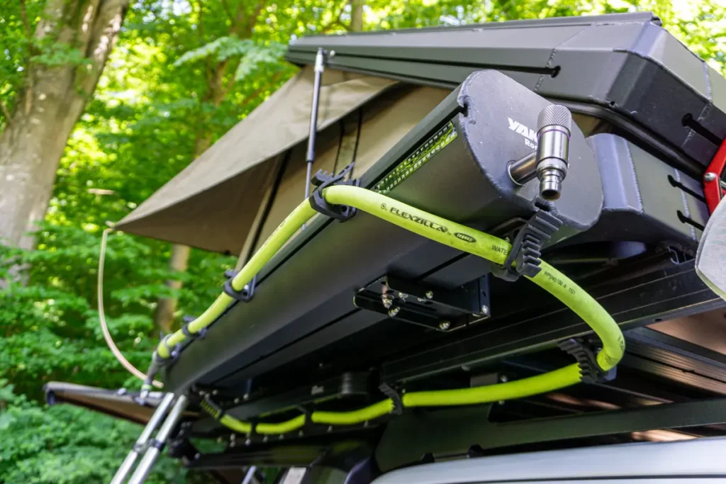 Dachzelt mit angebautem Wassersystem und flexiblen Wasserschlauch auf einem Overlanding-Fahrzeug im Grünen.