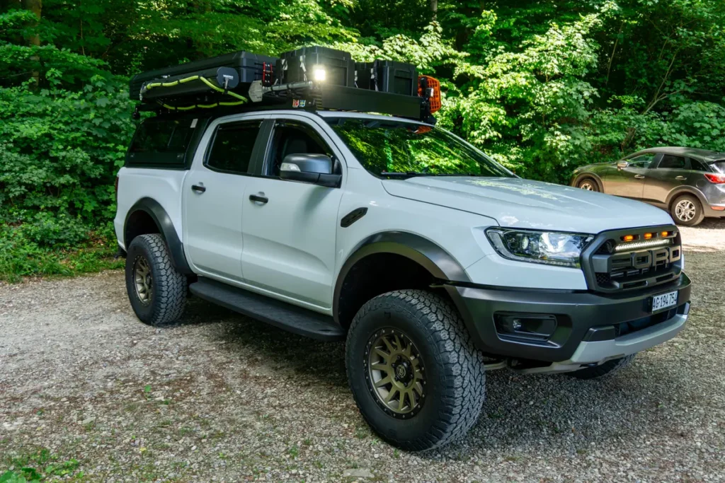 Weißer 4x4 Pick-up mit Dachzelt und umfangreicher Overlanding-Ausrüstung im Grünen.