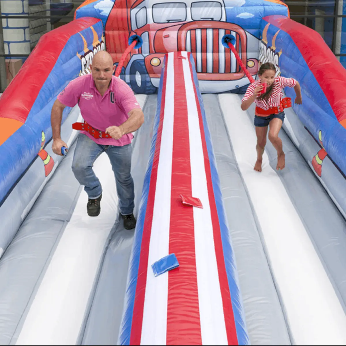 Ein Mann und ein Mädchen rennen auf einer aufblasbaren Bungee-Run-Bahn.