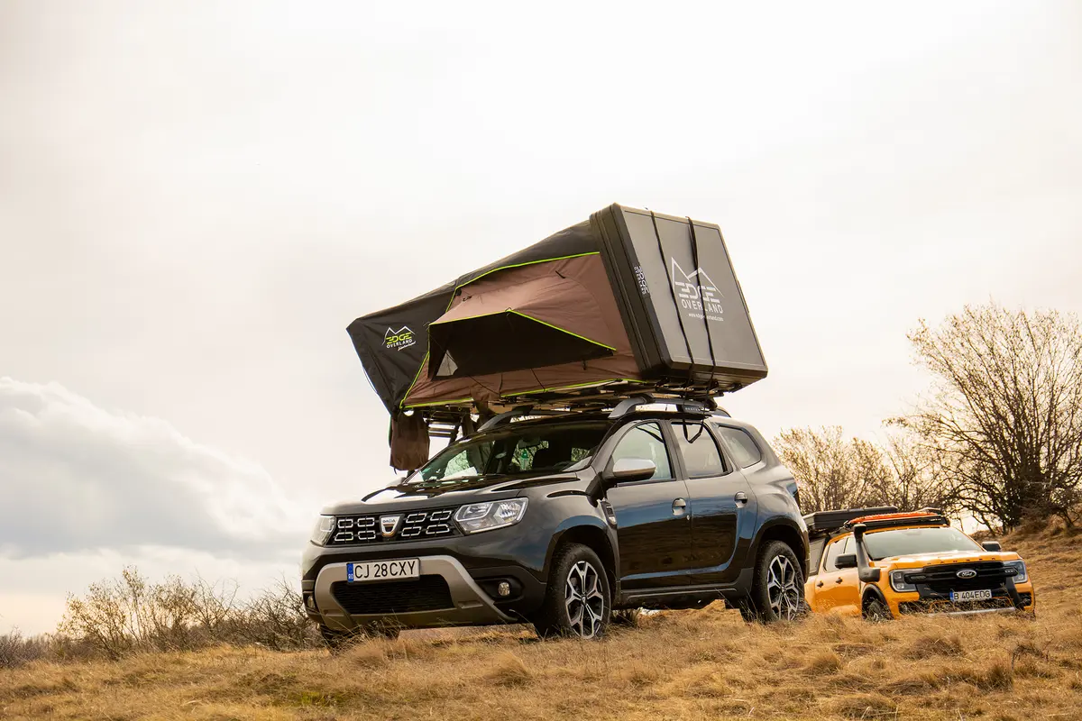 Dacia Duster 4x4 mit geöffnetem Dachzelt und ein gelber Ford Ranger Pick-up im trockenen Gelände.