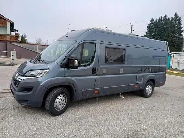 Ein moderner, grauer Kastenwagen-Campervan mit Hochdach und stilisierten Bergen an der Seite.