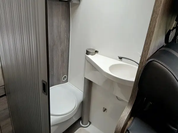 Innenansicht eines kompakten Campervan-Badezimmers mit Toilette und Waschbecken.