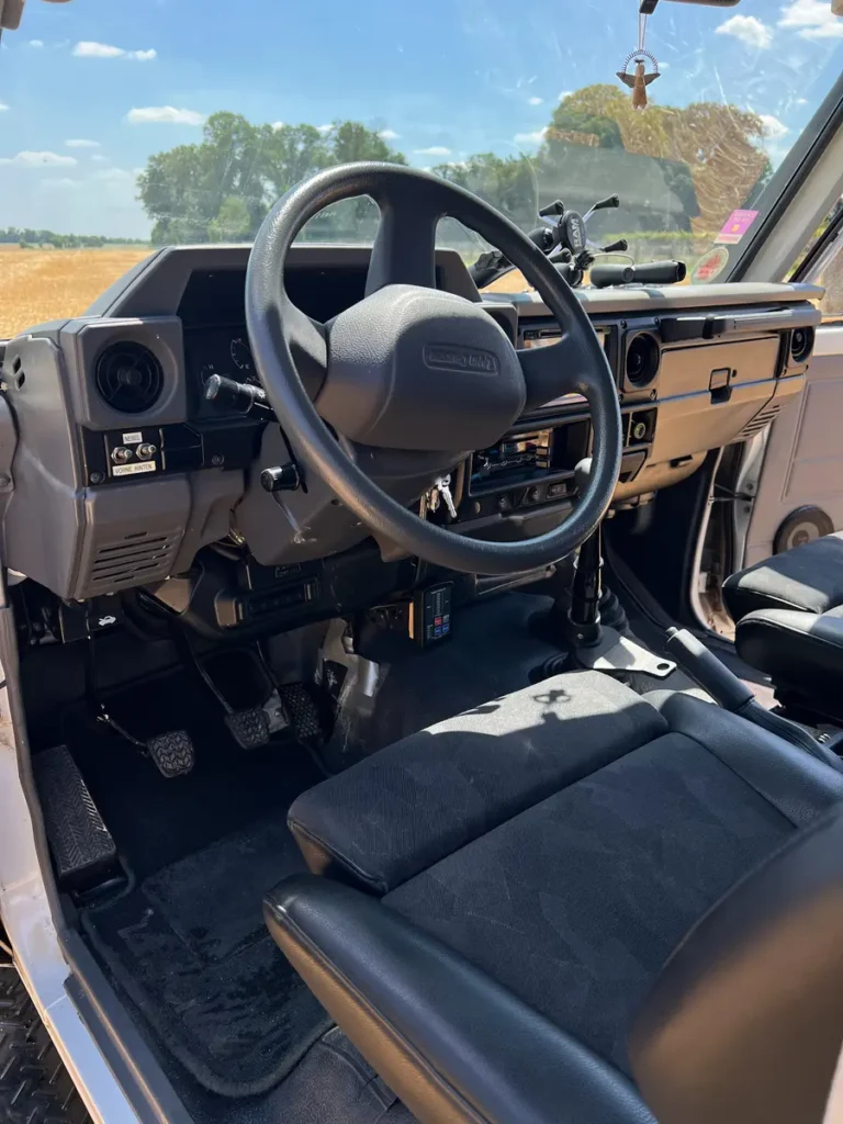 Innenansicht eines 4x4 Geländewagens mit Lenkrad, Armaturenbrett und Schaltgetriebe, Blick auf ein Feld.