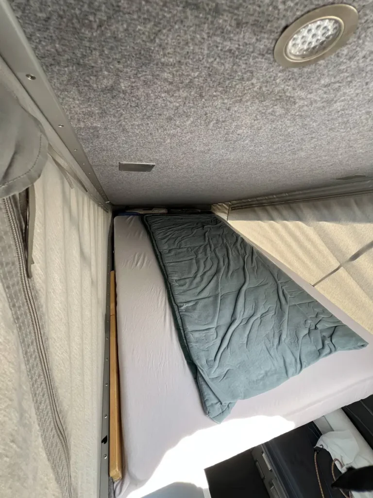 Gemütliche Schlaffläche in einem Campervan mit Filzverkleidung und LED-Deckenleuchte.