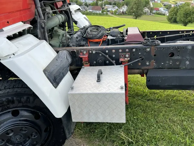 Robustes LKW-Fahrgestell mit montierter Riffelblech-Staubox, Reifen und Federungselementen auf grünem Gras.