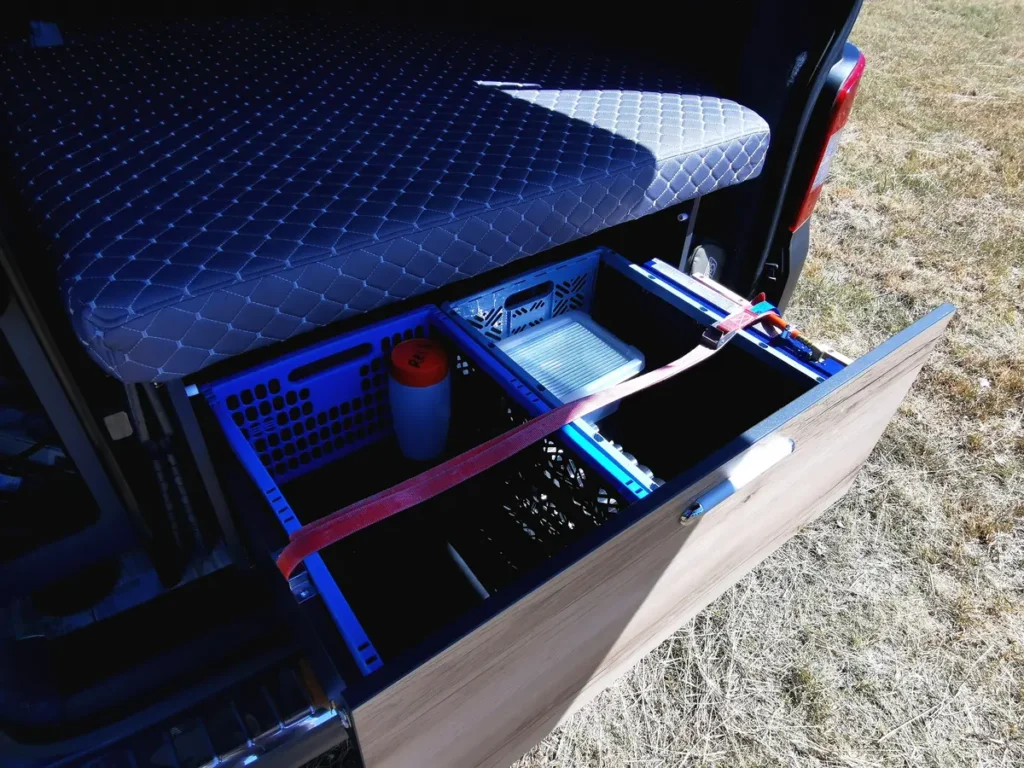 Ausziehbarer Stauraum mit Ordnungsboxen unter dem Bett in einem Campervan-Selbstausbau.